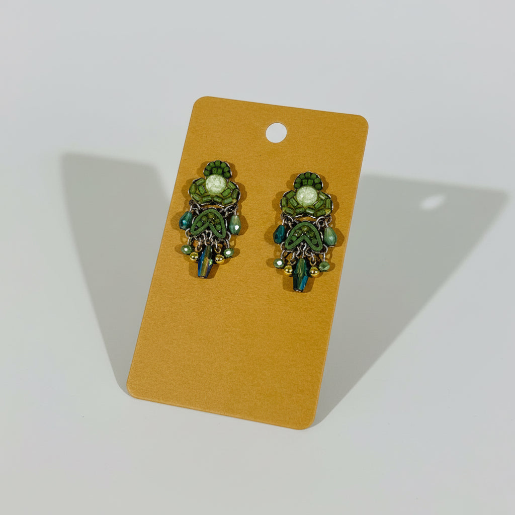 Pair of green earrings on a beige card against a textured white background
